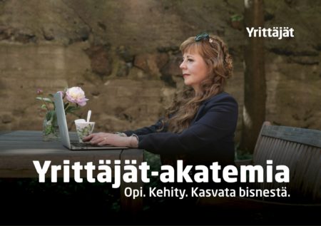 nainen istuu pöydän ääressä ja hänen kätensä ovat auki olevan läppärin näppäimistöllä
